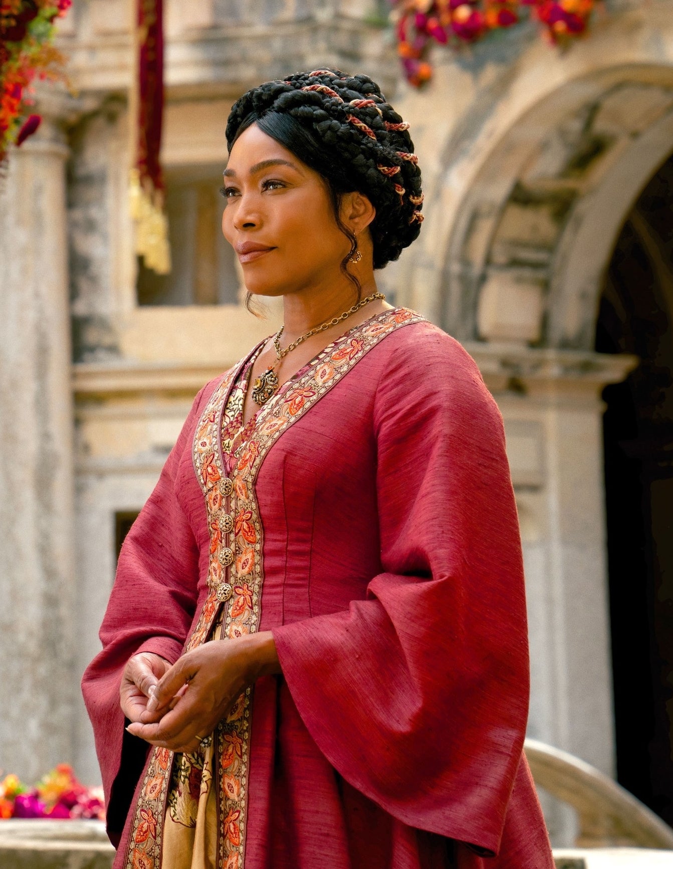 Angela Basset in medieval attire stands in a courtyard with floral arrangements in a from Damsel