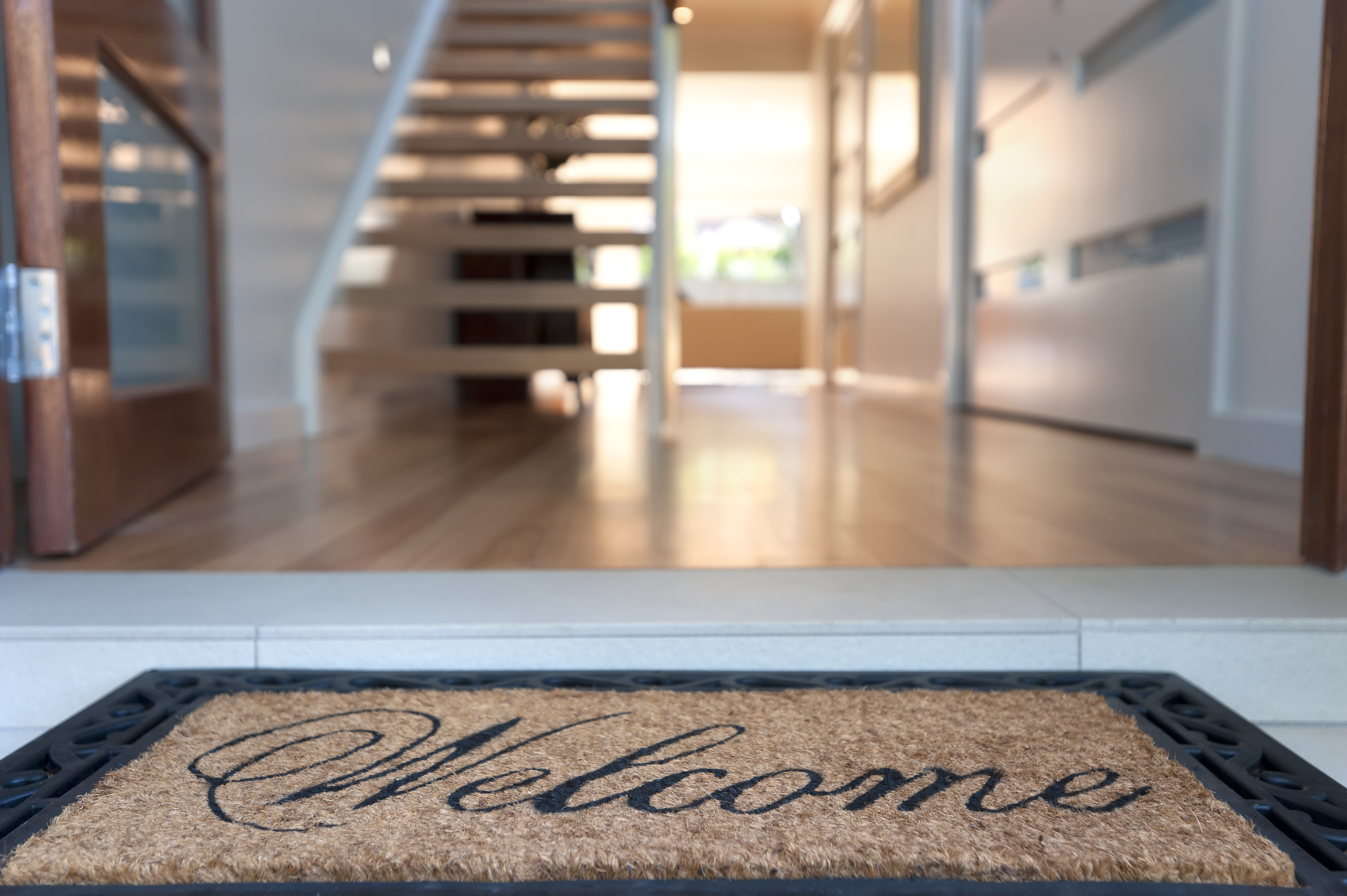 A welcome mat at the threshold of an open doorway leading to a modern interior with stairs with no railing