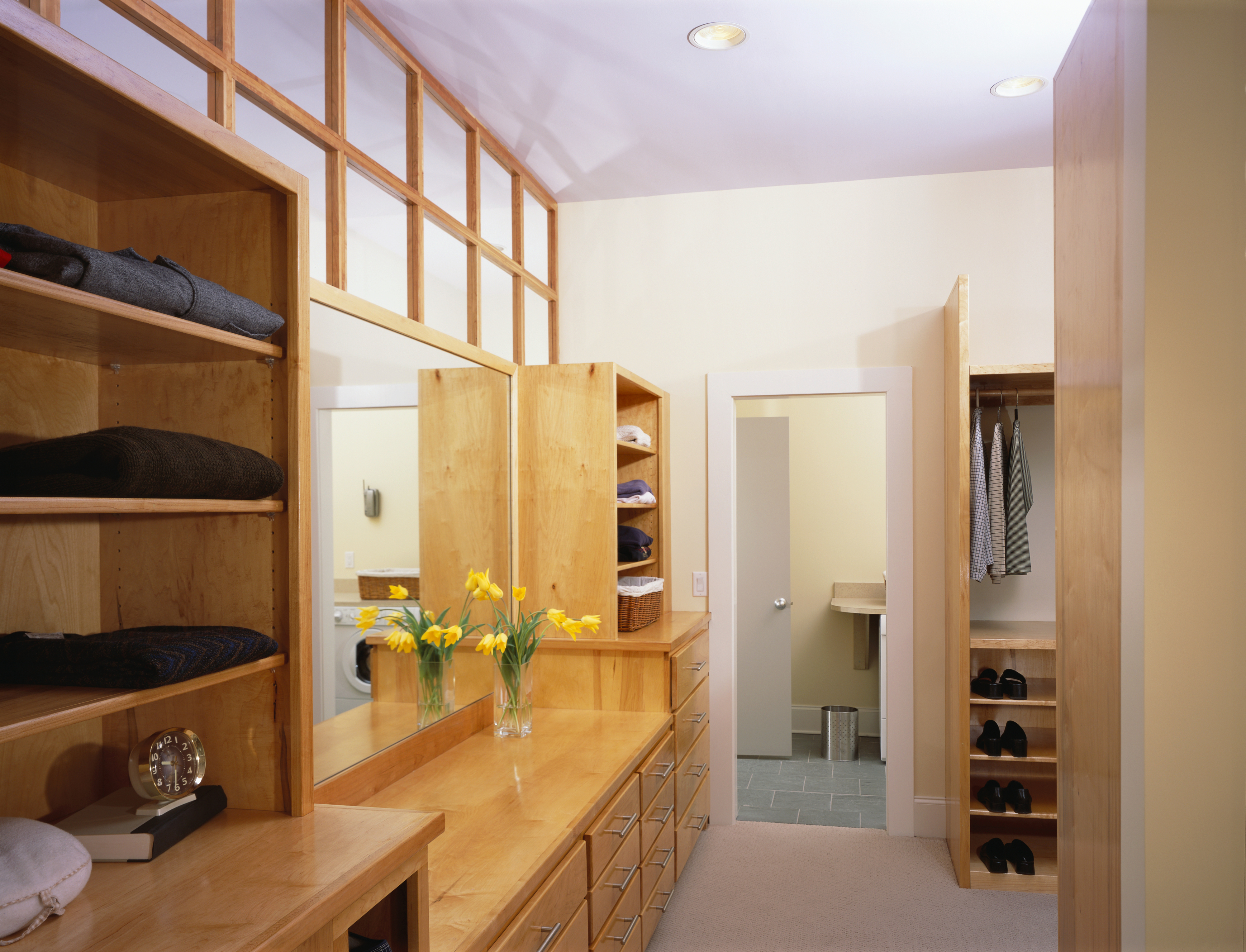 Walk-in closet with built-in wooden cabinets, shelves for shoes and clothes, a vanity area, and a bathroom entrance