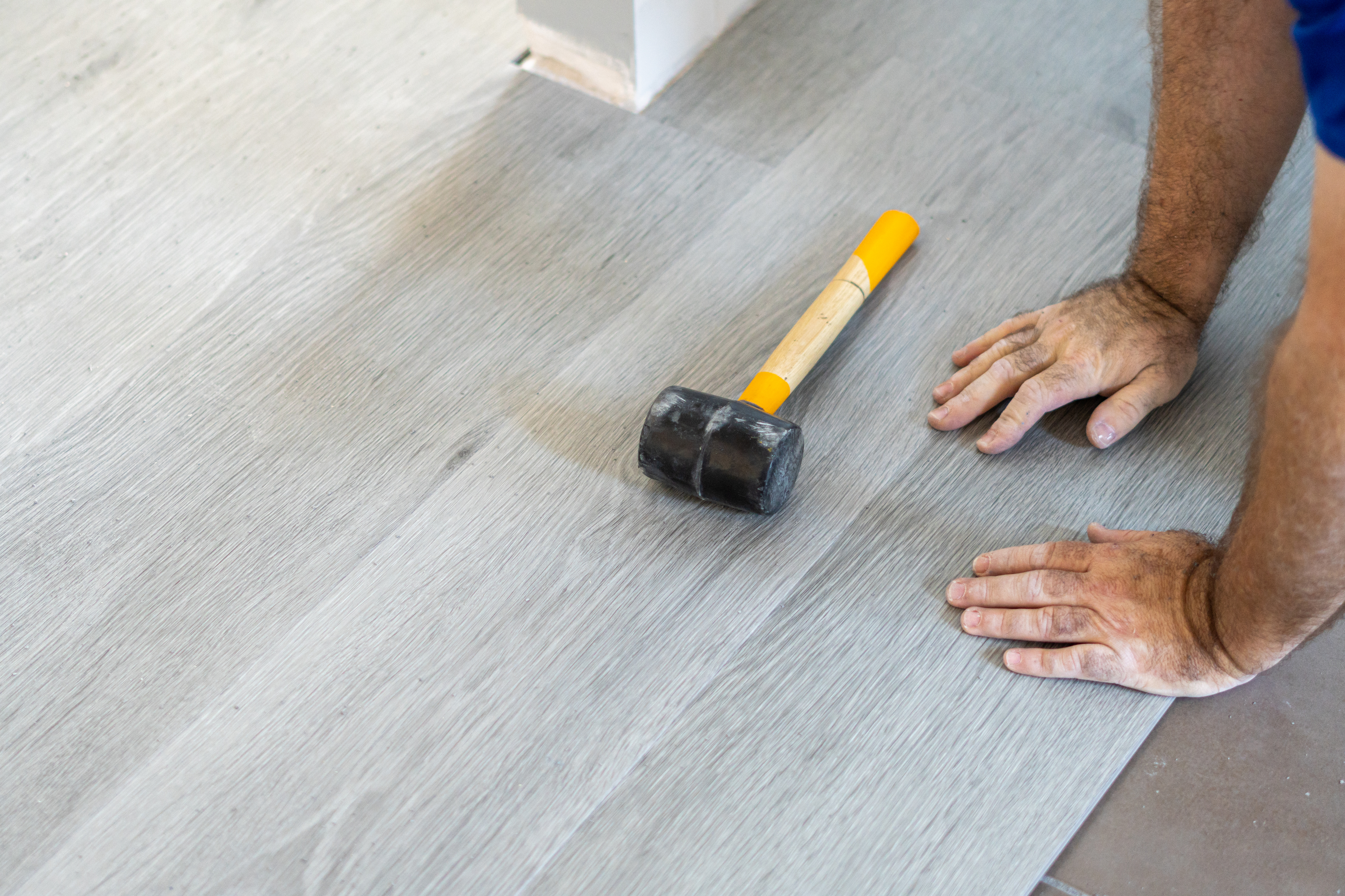 Person installing flooring with a mallet nearby