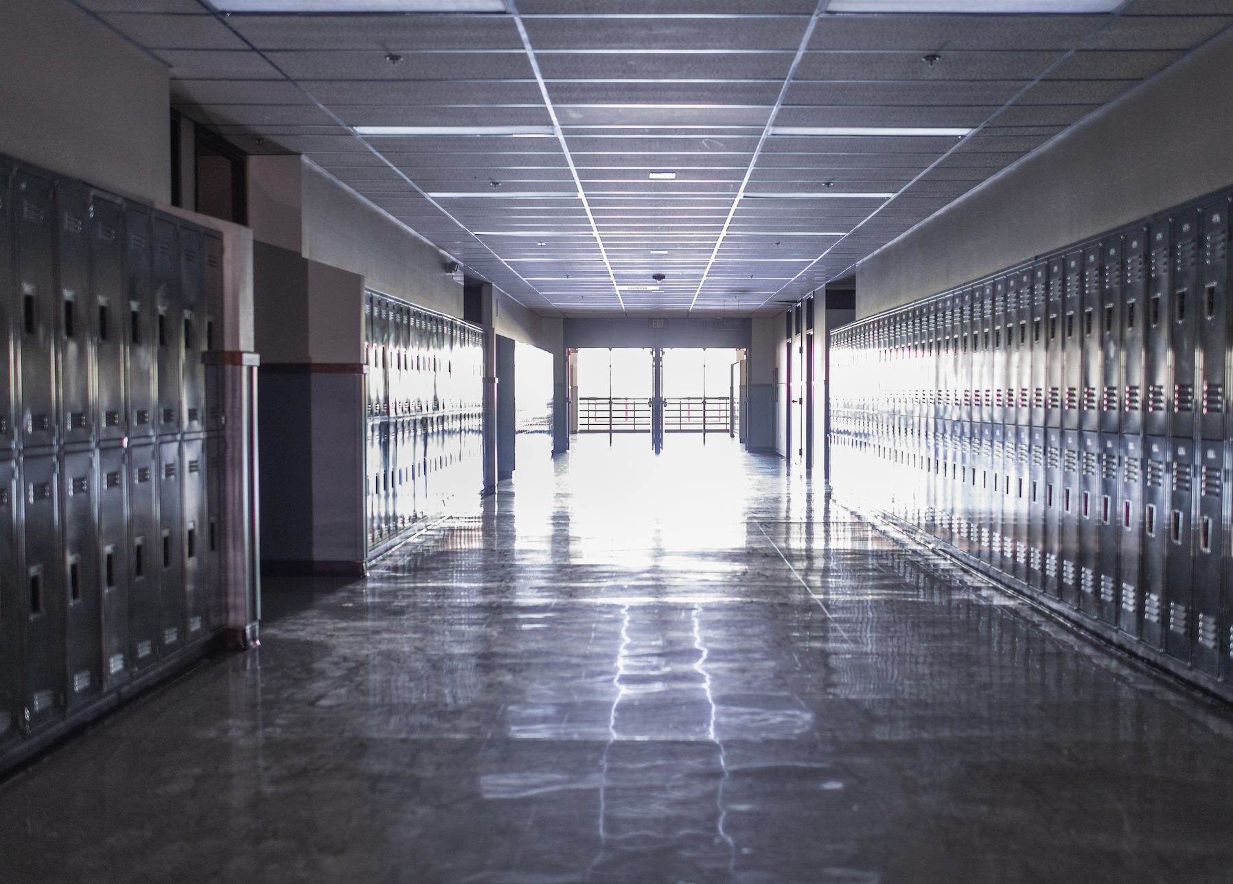Empty school hallway with rows of lockers on both sides, sunlight streaming in from the end