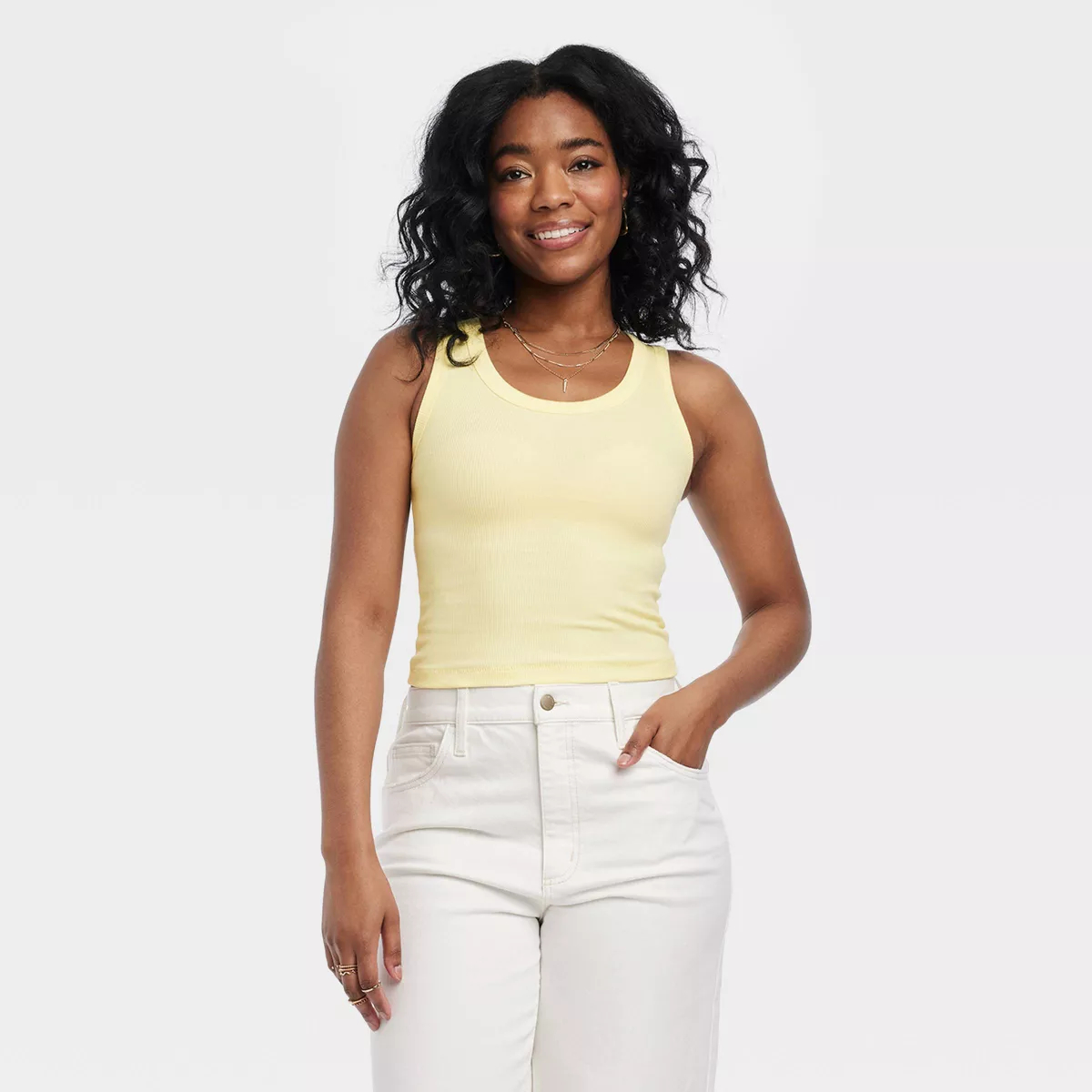 Model in sleeveless top and white pants posing. Shopping for contemporary casual wear.
