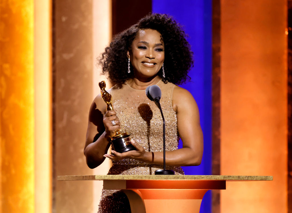 Angela Basset in sparkling gown holding her honorary Oscar as she smiles and stands at a podium