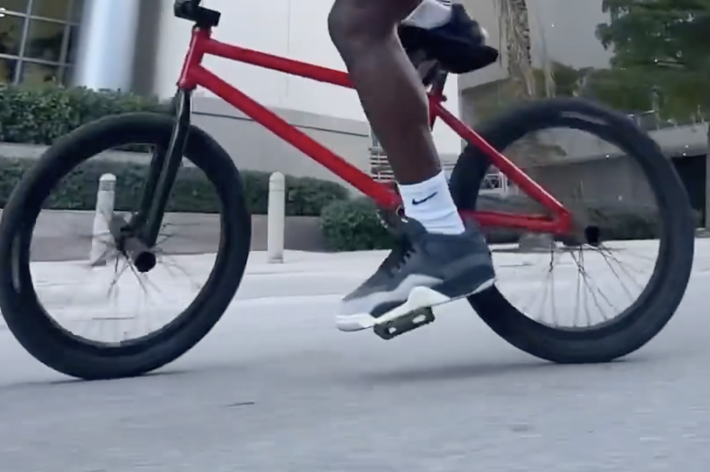 Close-up of a person riding a bike, wearing distinctive sneakers, focus on the shoes' design and brand