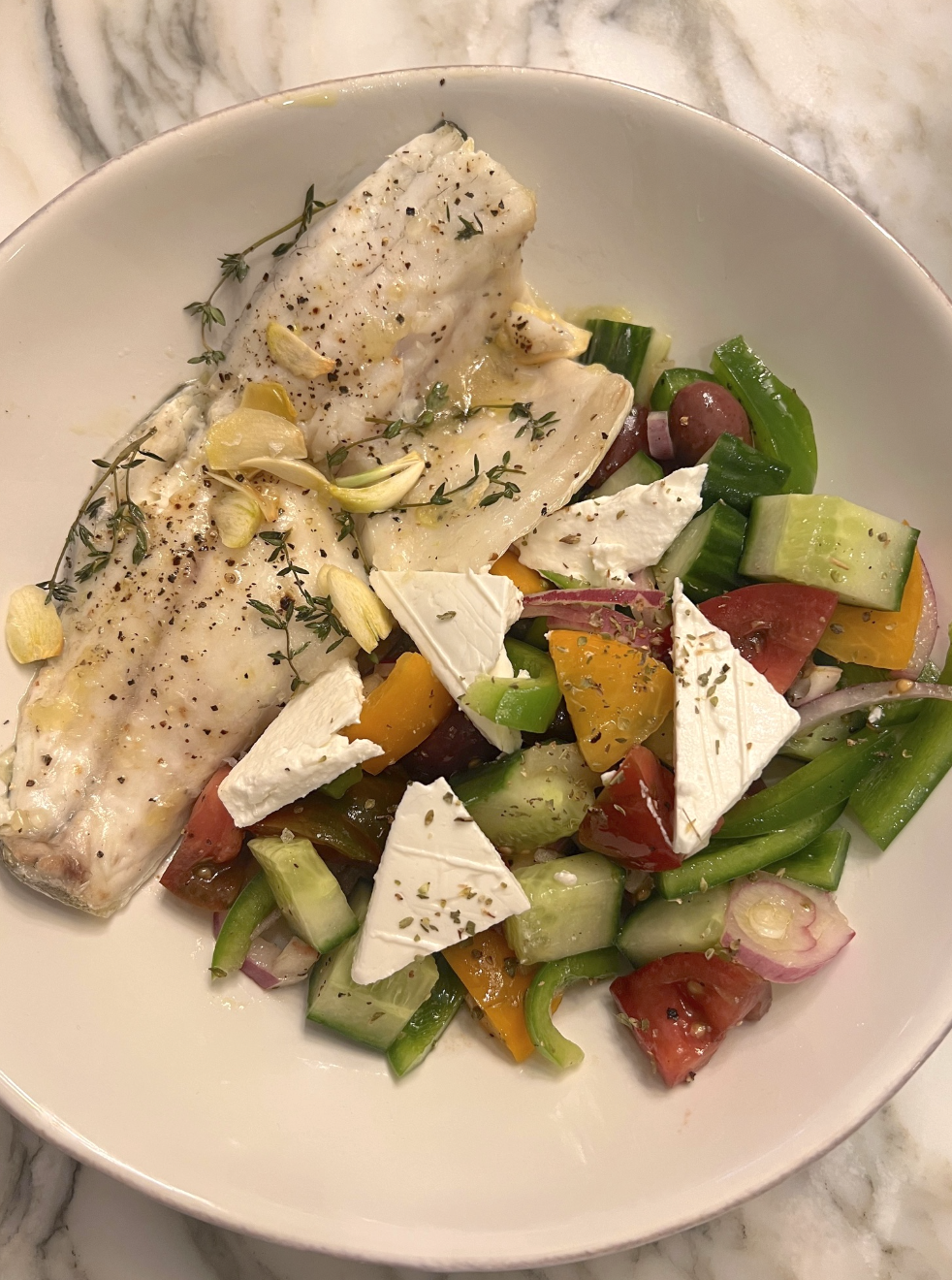 Plate with fish and Greek salad with feta cheese, olives, cucumber, onion, and bell peppers