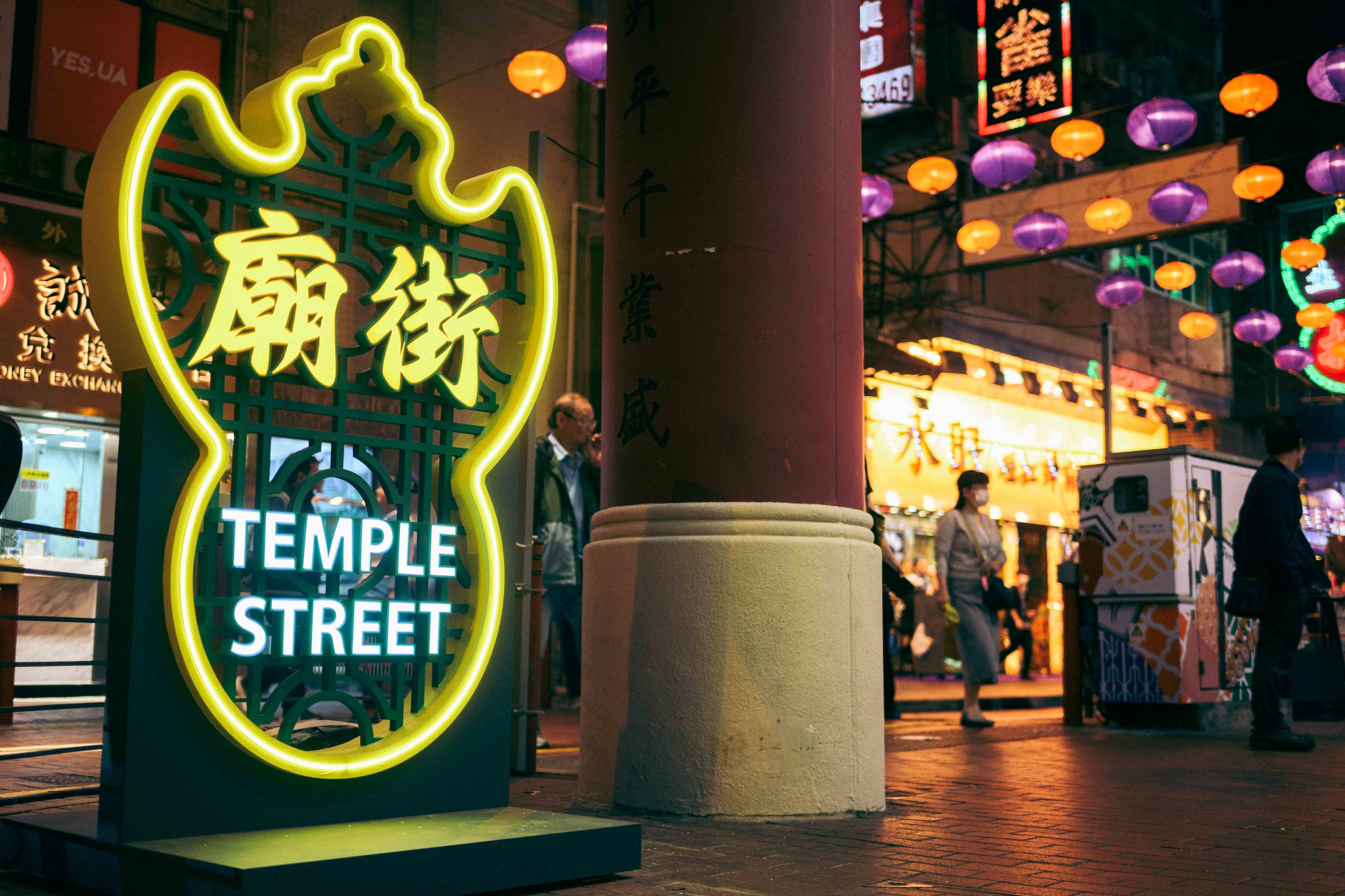Neon sign for Temple Street with Chinese characters, at a busy evening market street