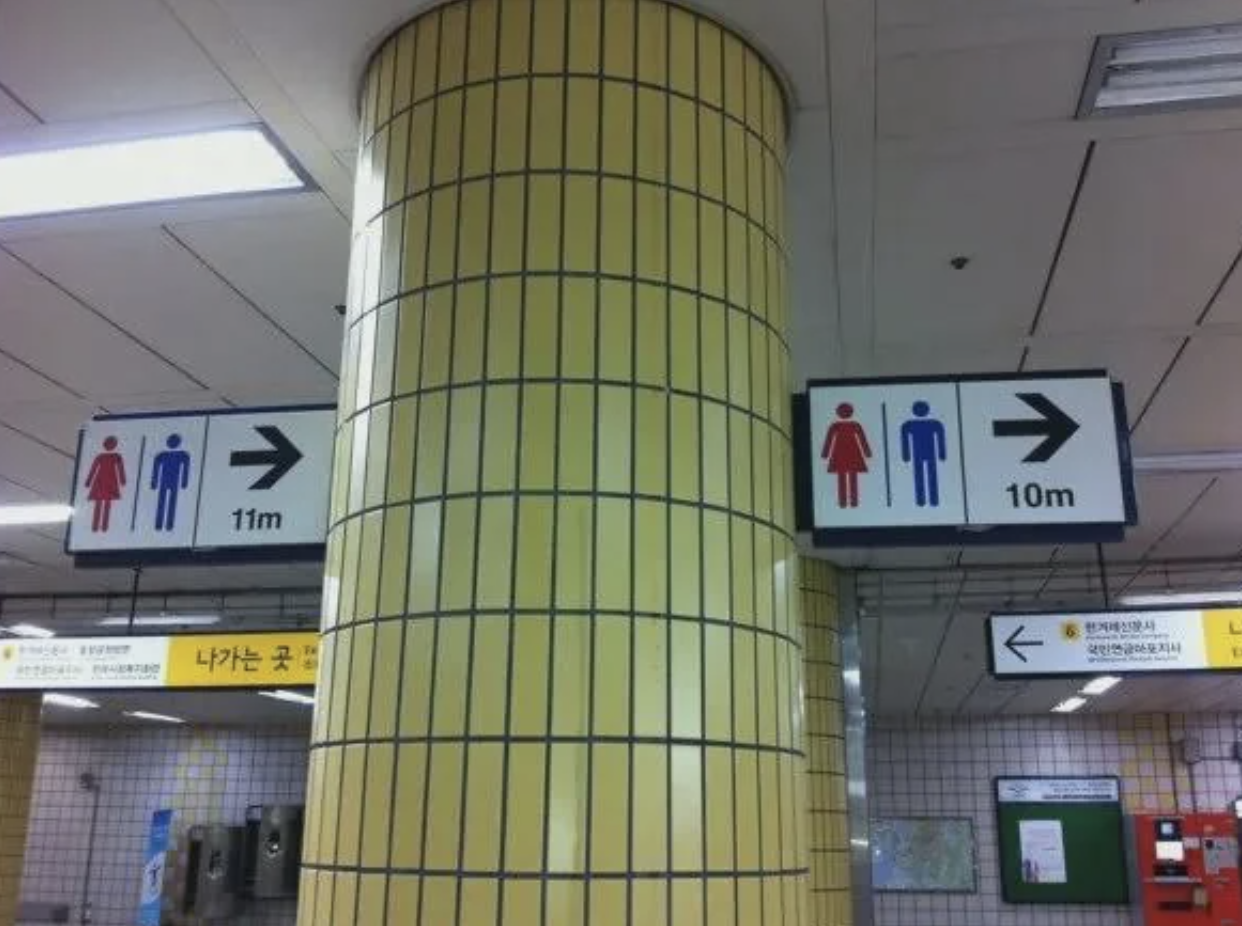 Signs in a subway station indicating restrooms, with conflicting arrow distances (from 10 meters to 11 meters)