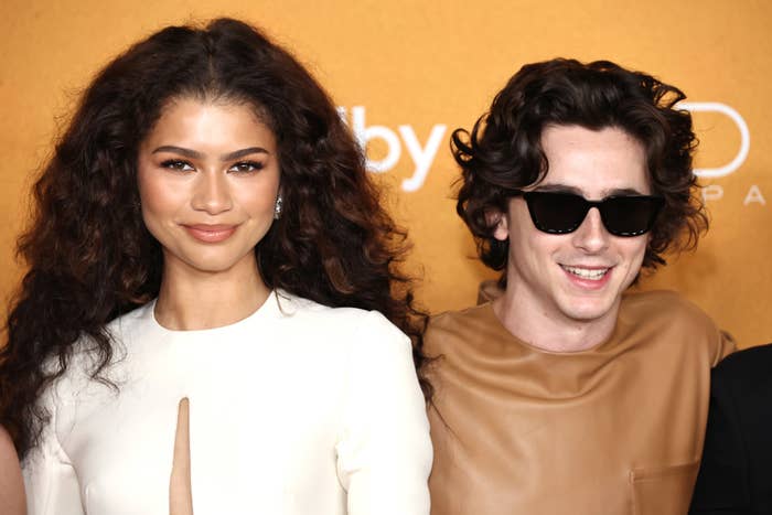 Zendaya in a white dress with a keyhole neckline next to Timothée in a tan suit and black sunglasses