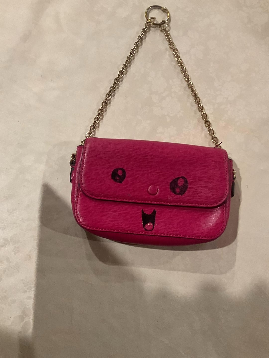 Small pink purse with a chain strap and facial features resembling a cat