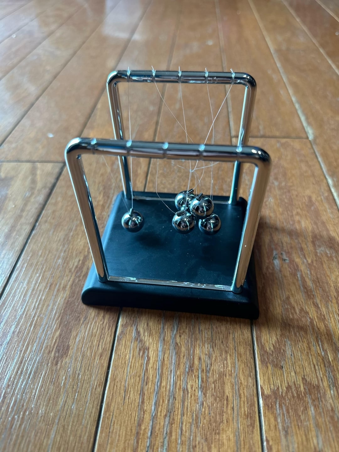 Newton&#x27;s cradle with balls in motion on a wooden floor