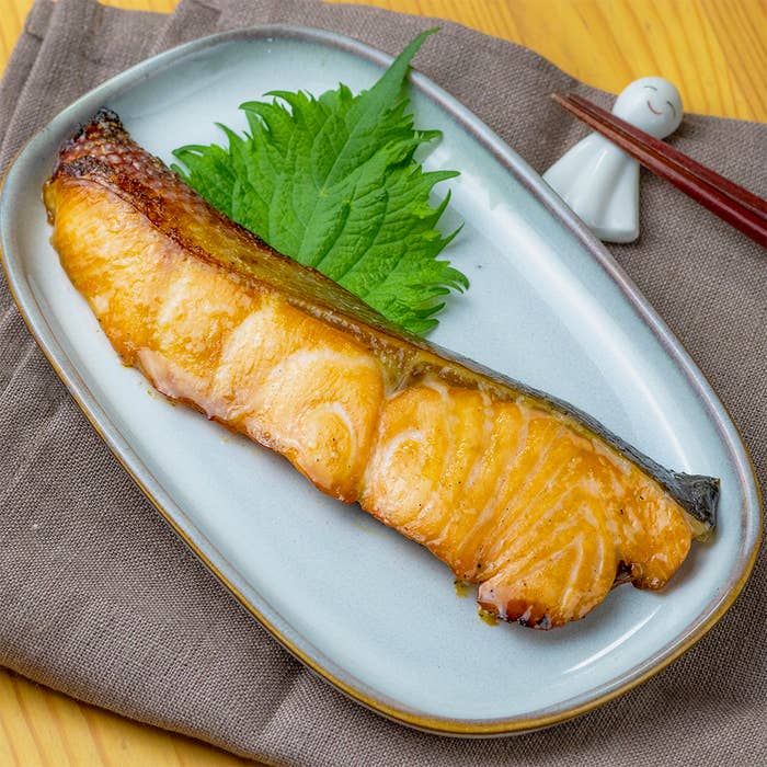 焼き魚が皿に盛られており、添えられた緑の葉と箸が見えます。