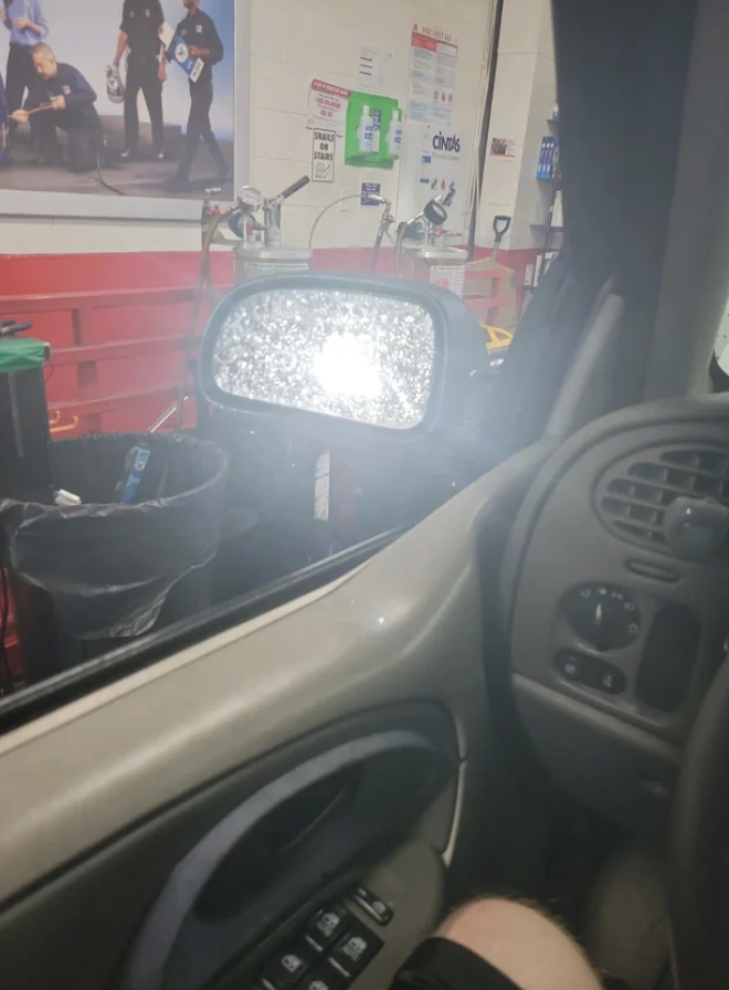 Car side mirror covered with snow reflecting light, with a glimpse of a garage interior