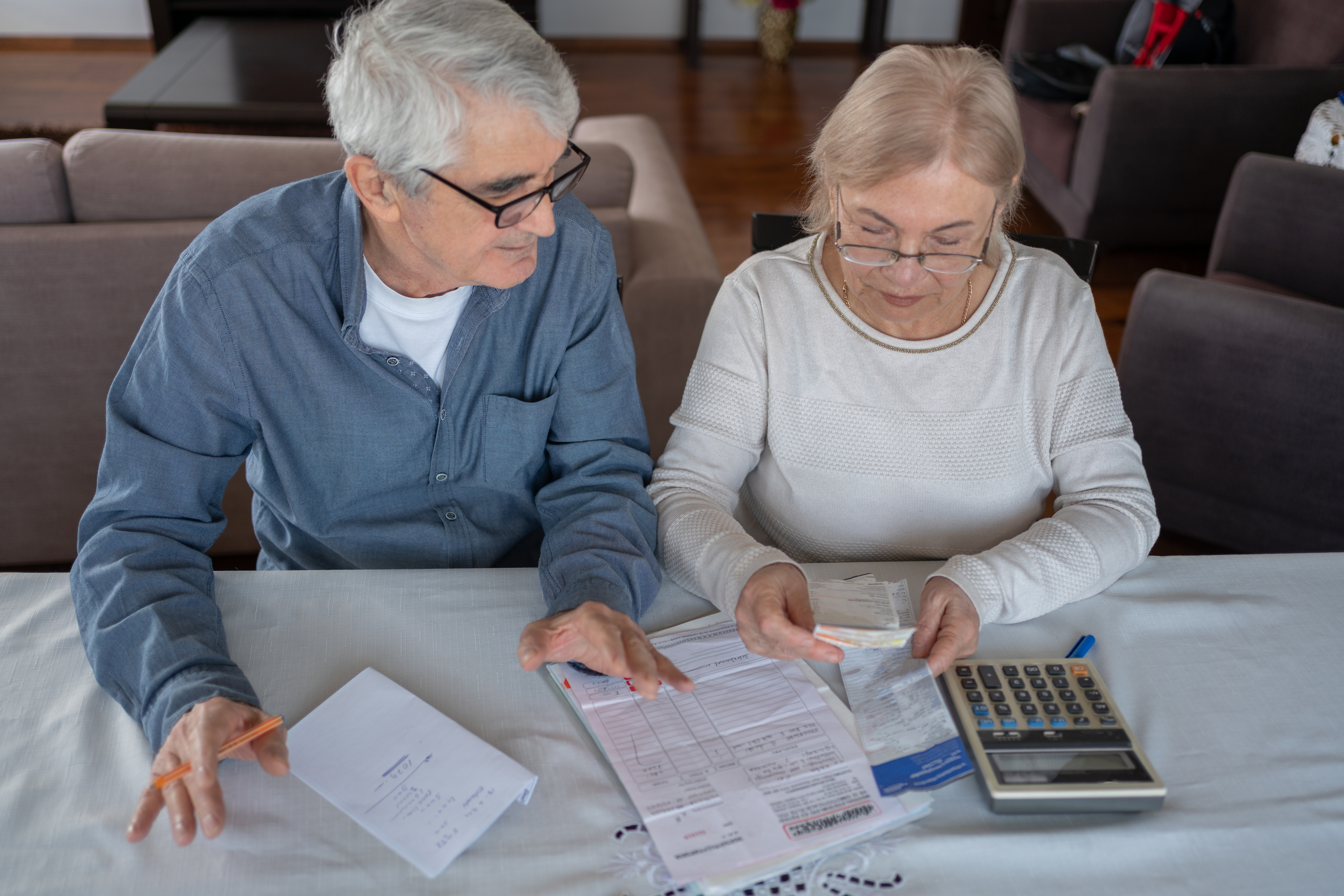 Two elderly individuals reviewing documents at a table, with calculator and medications nearby