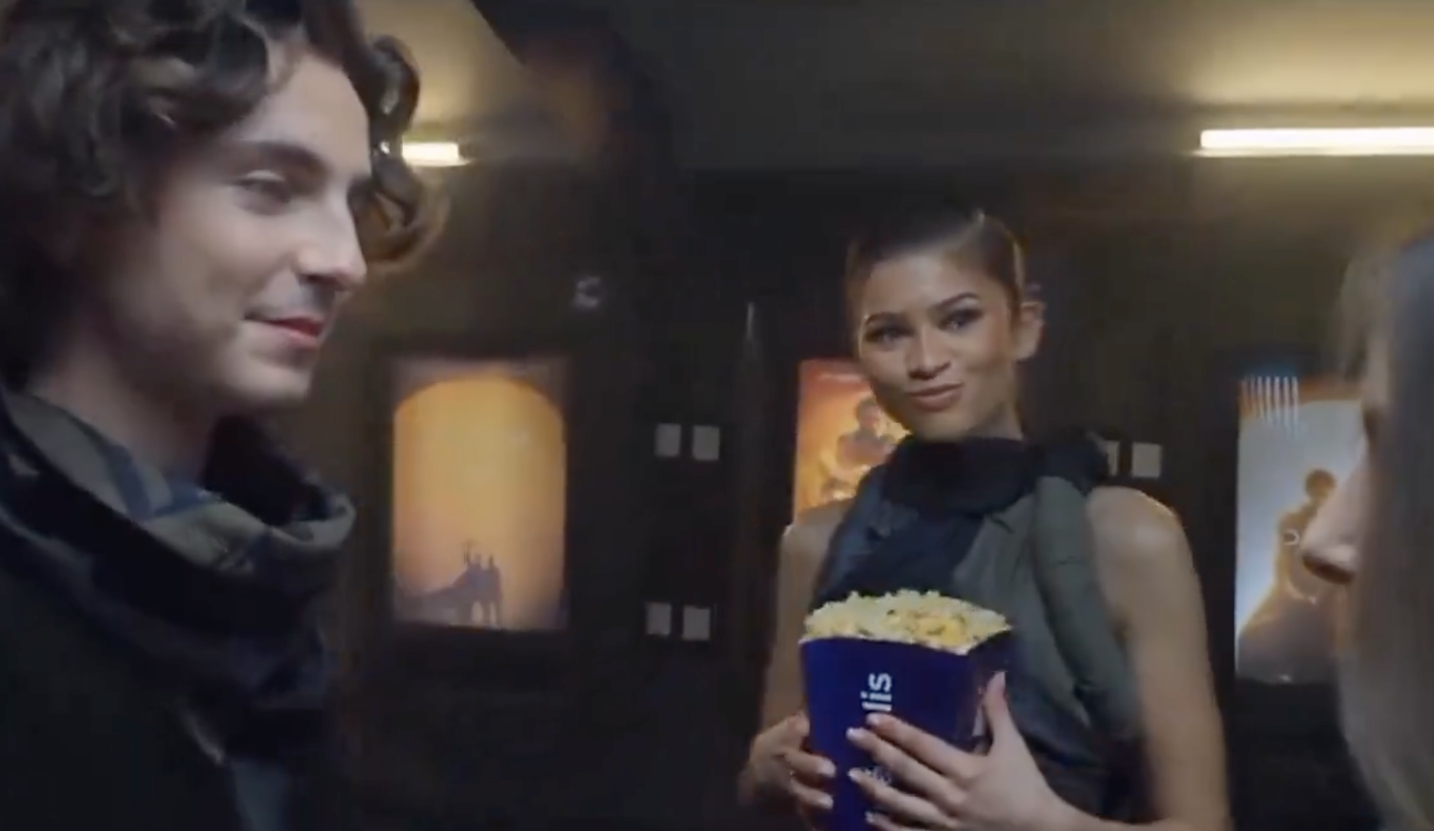 Timmy and Zendaya in a movie theater scene looking at another actor, with Zendaya holding a tub of popcorn