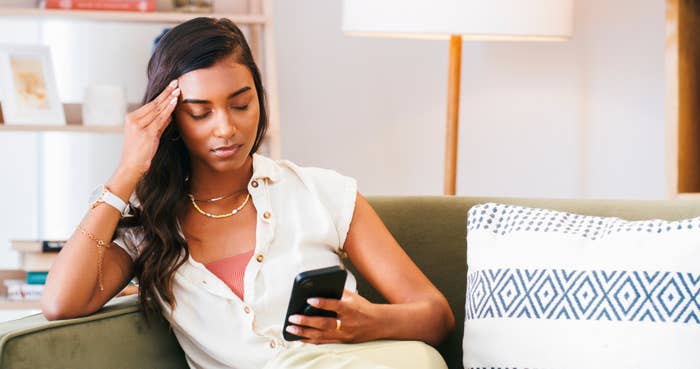 Person looking at phone with a concerned expression while sitting on a couch