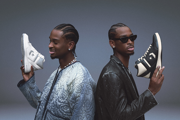 Two individuals showing off sneakers, one holding a white pair, the other a black pair, with a focus on the footwear design