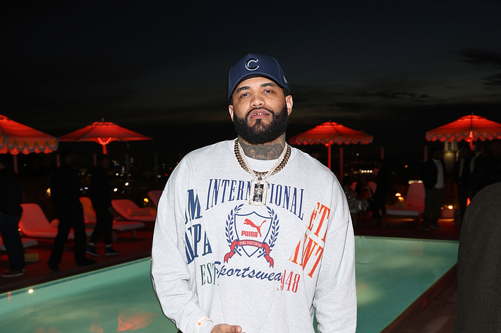 Man in branded sweatshirt and cap standing by a pool at an evening event