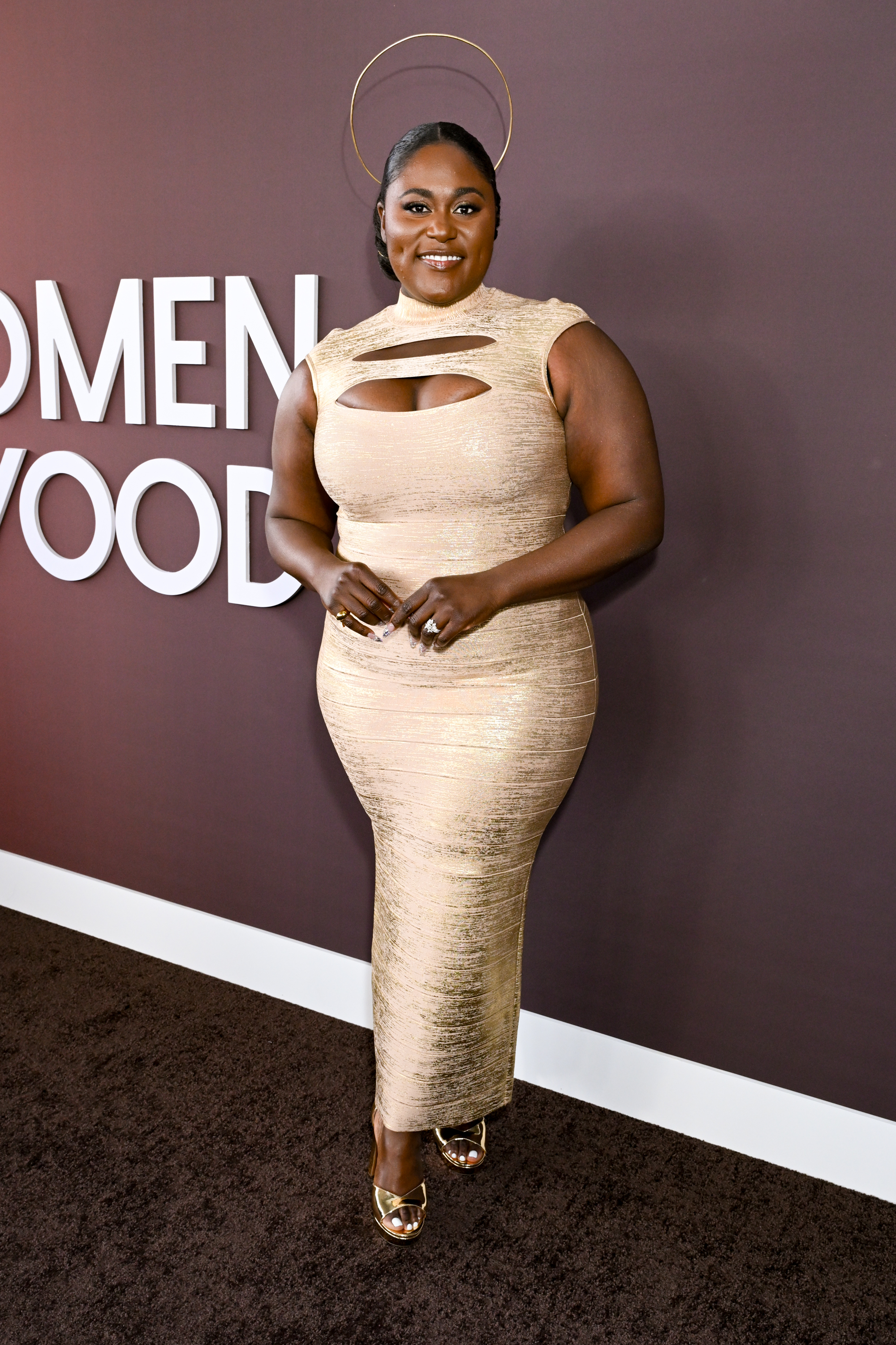 Danielle Brooks poses in a cut-out sleeveless gown at an event with a halo headpiece