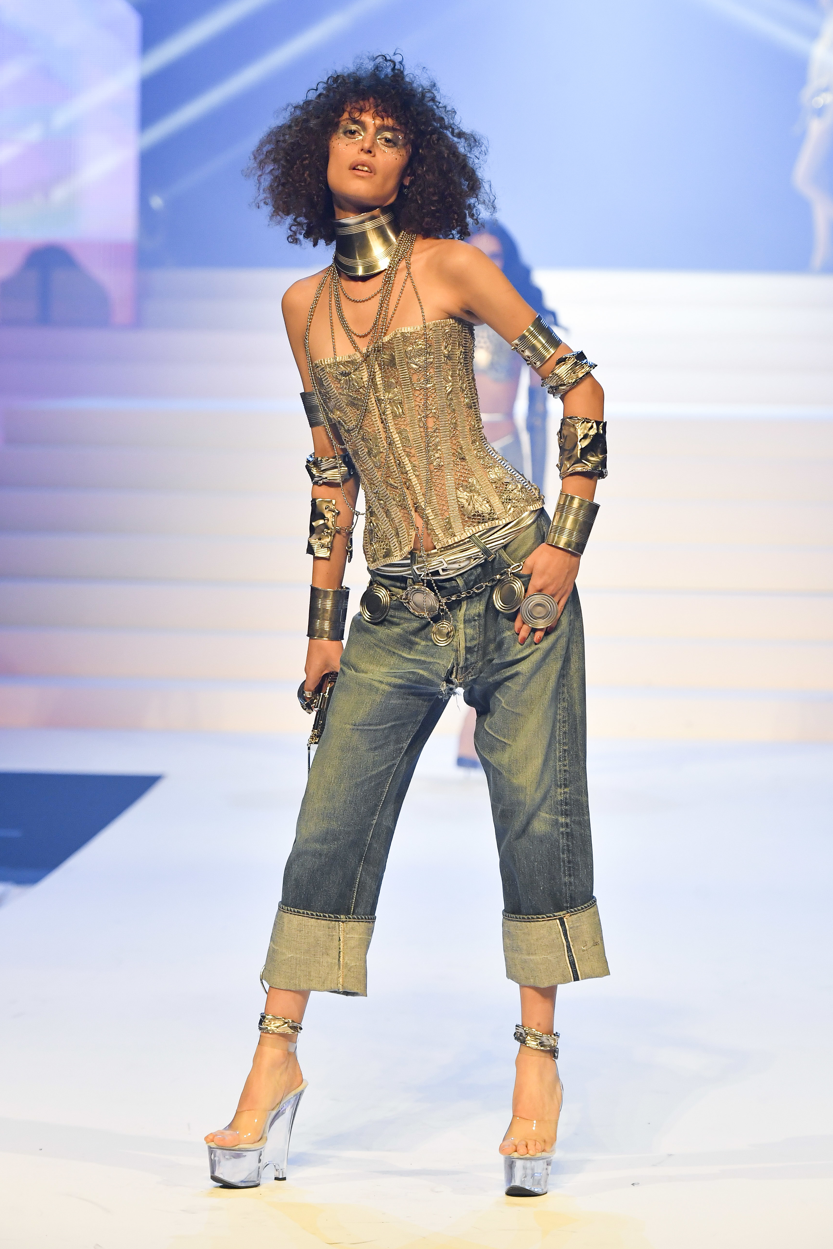 Model on runway in metallic corset top, cropped jeans, platform heels, and lots of bangles
