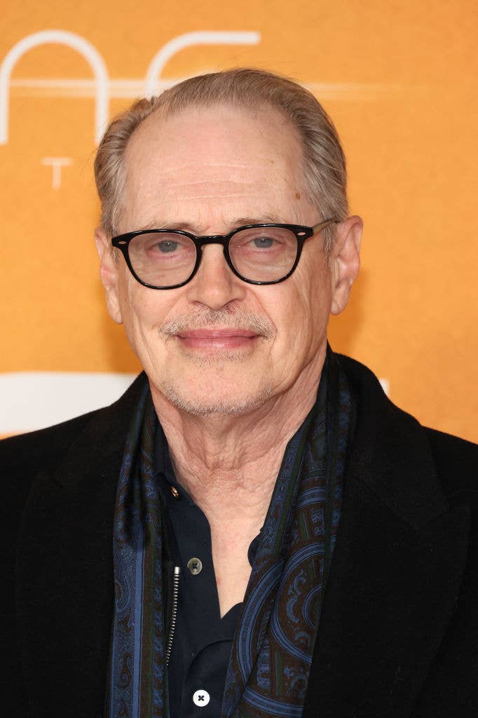 Man in glasses and a black layered outfit with a patterned scarf at an event