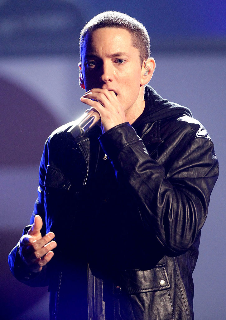 Eminem performing on stage, wearing a leather jacket, with a microphone in hand