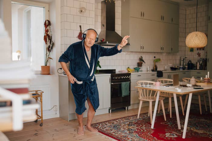 Man in a robe wearing headphones and dancing to music in a kitchen