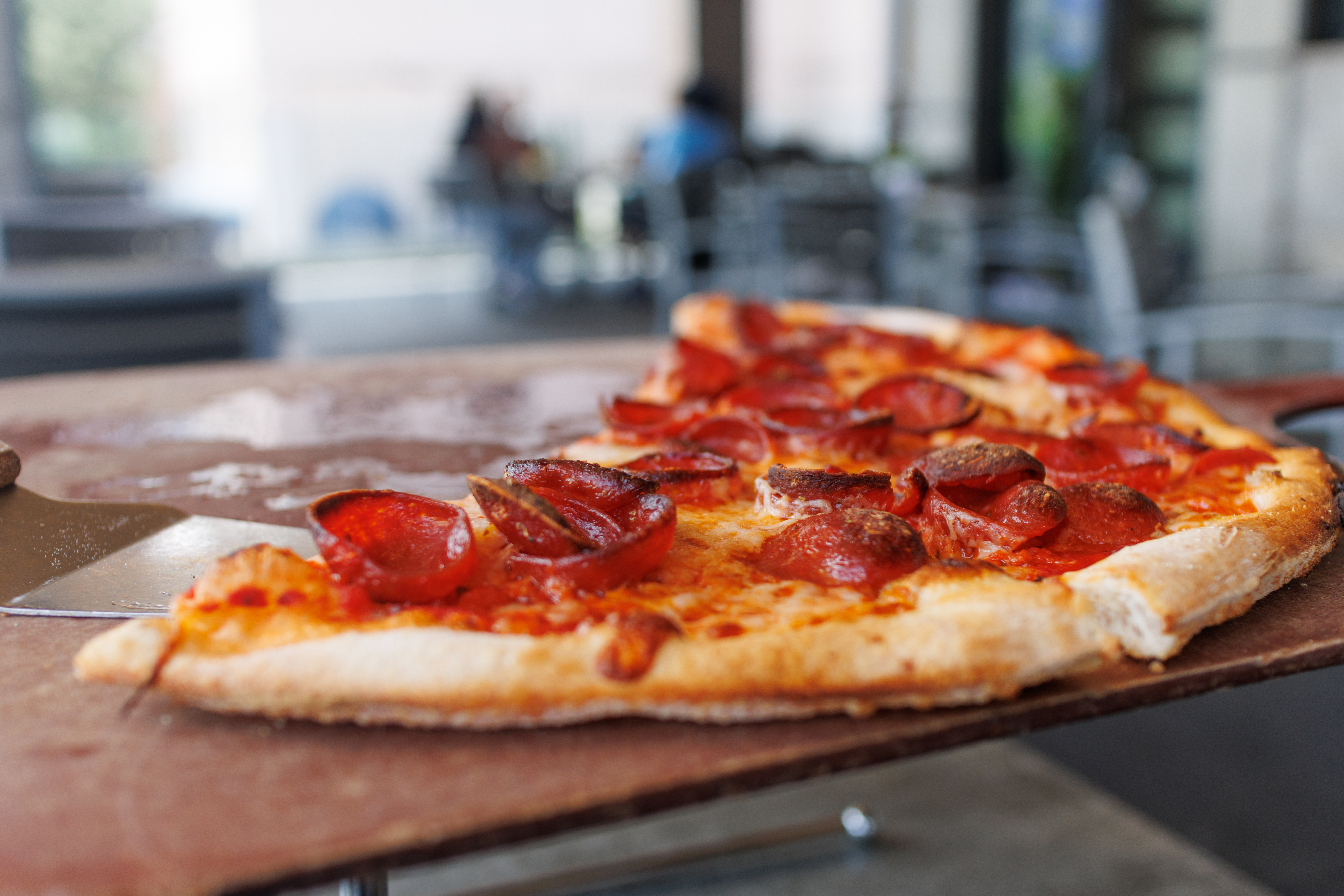 A pepperoni pizza with a visibly crispy crust sits on a wooden peel, ready to be served. No people in image