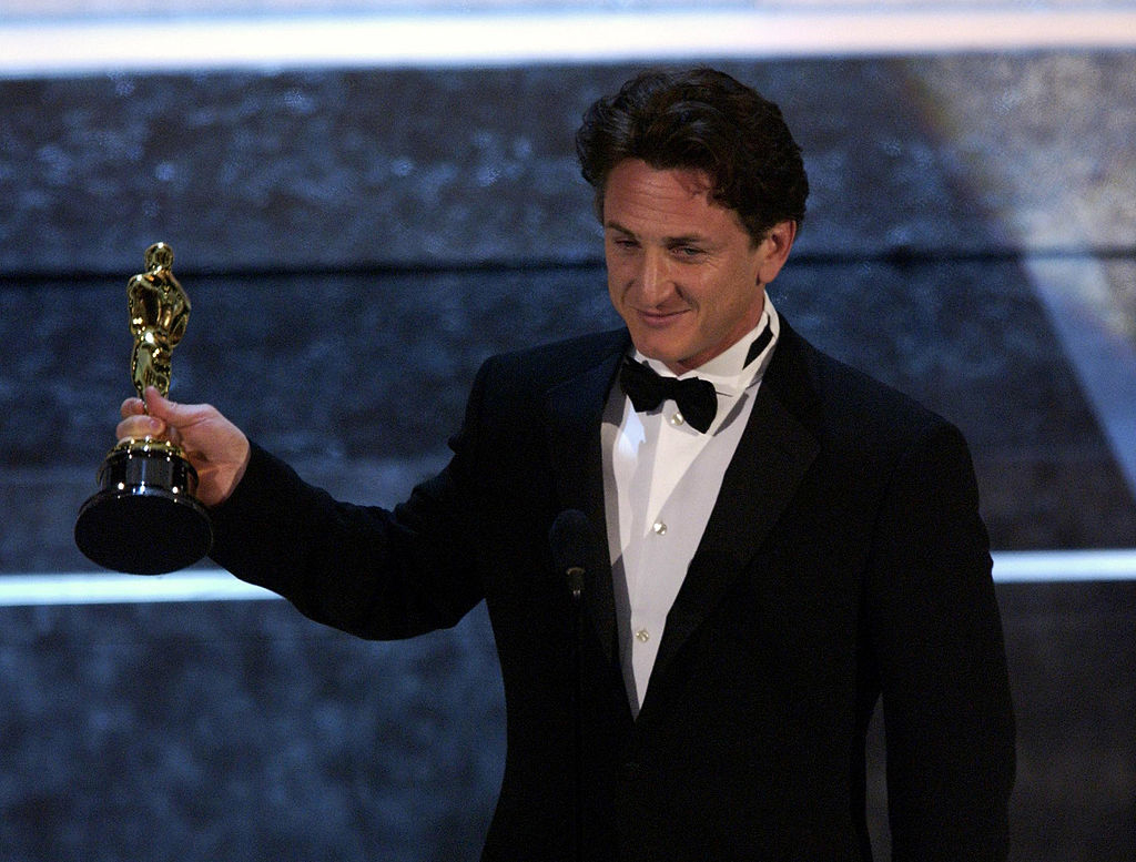 Sean holding an Oscar award onstage, smiling, and wearing a tuxedo with a bow tie