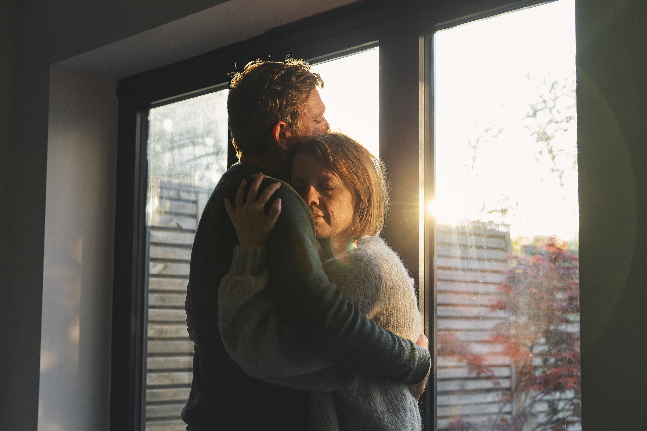 Two individuals embracing affectionately by a window with sunlight coming through