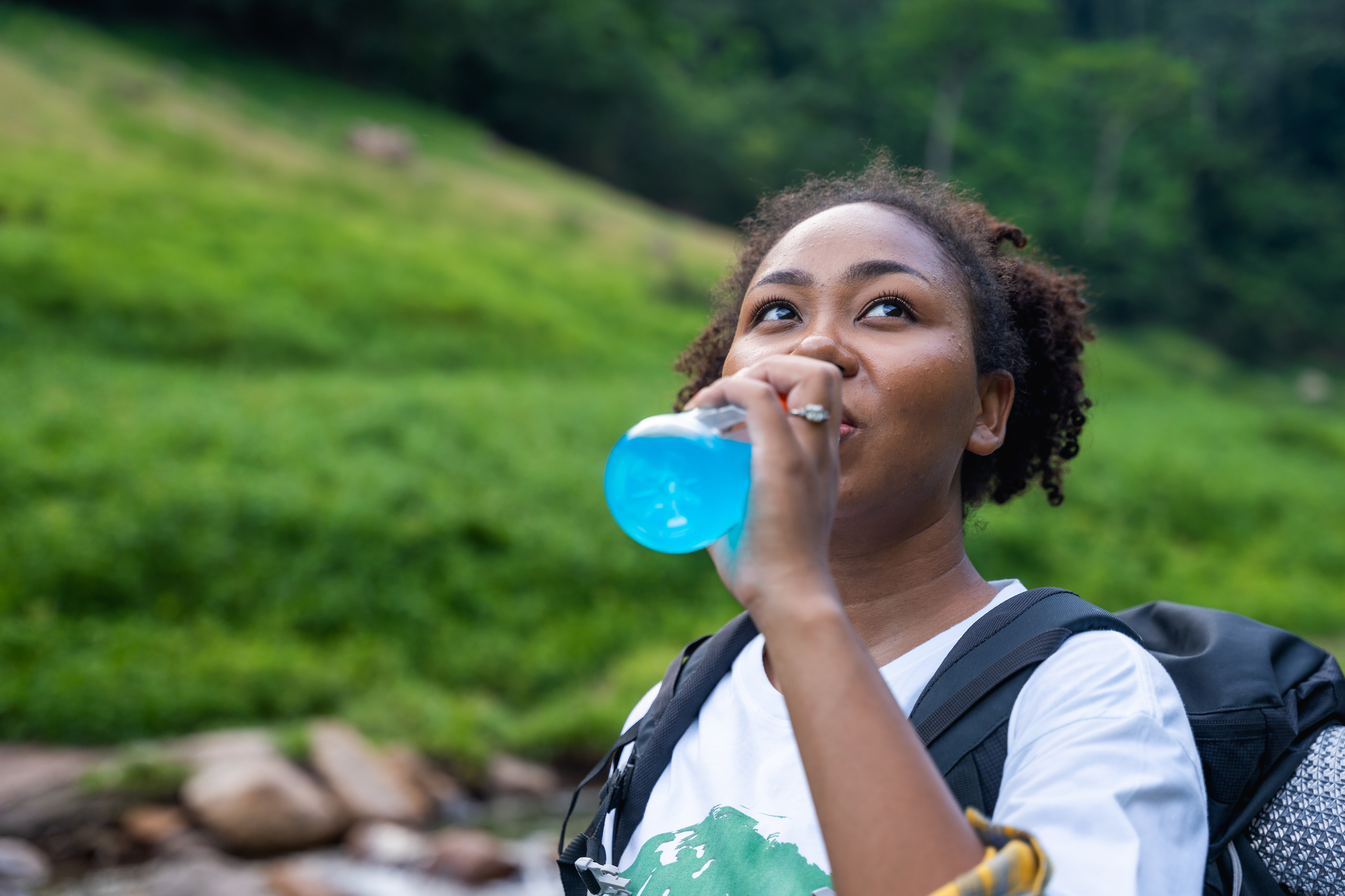 Person drinking water from a bottle outdoors with a backpack, in a natural setting