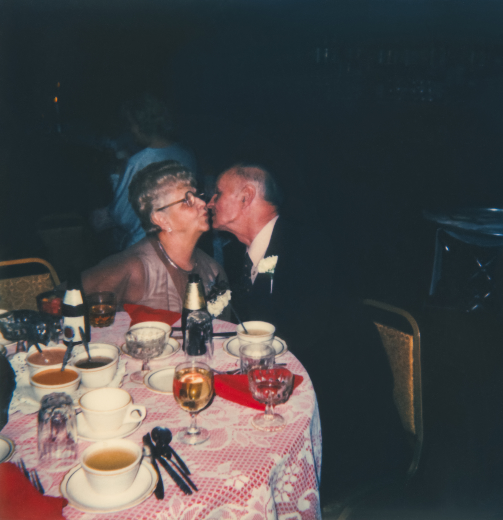 Older couple sharing a kiss at a dining table set with cups and dishes