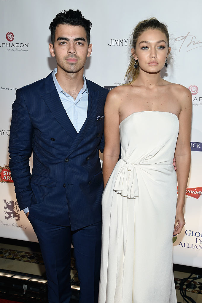 Joe Jonas and Gigi Hadid standing together; Joe in a suit and Gigi in a strapless dress
