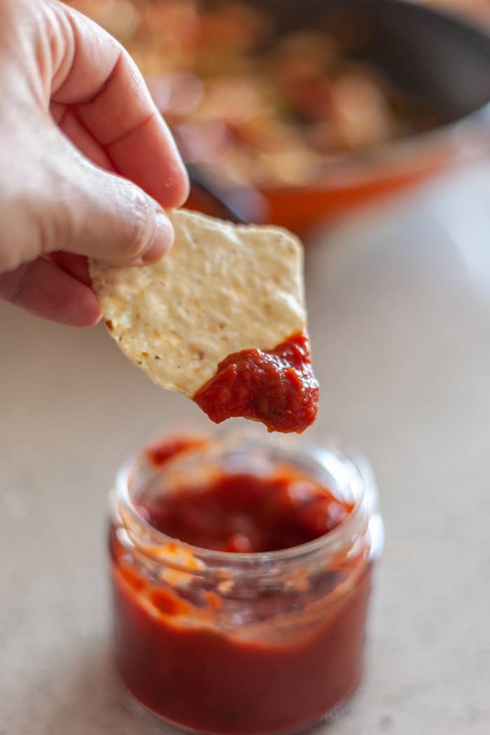 Hand dipping a chip into a jar of salsa with a pot in the background