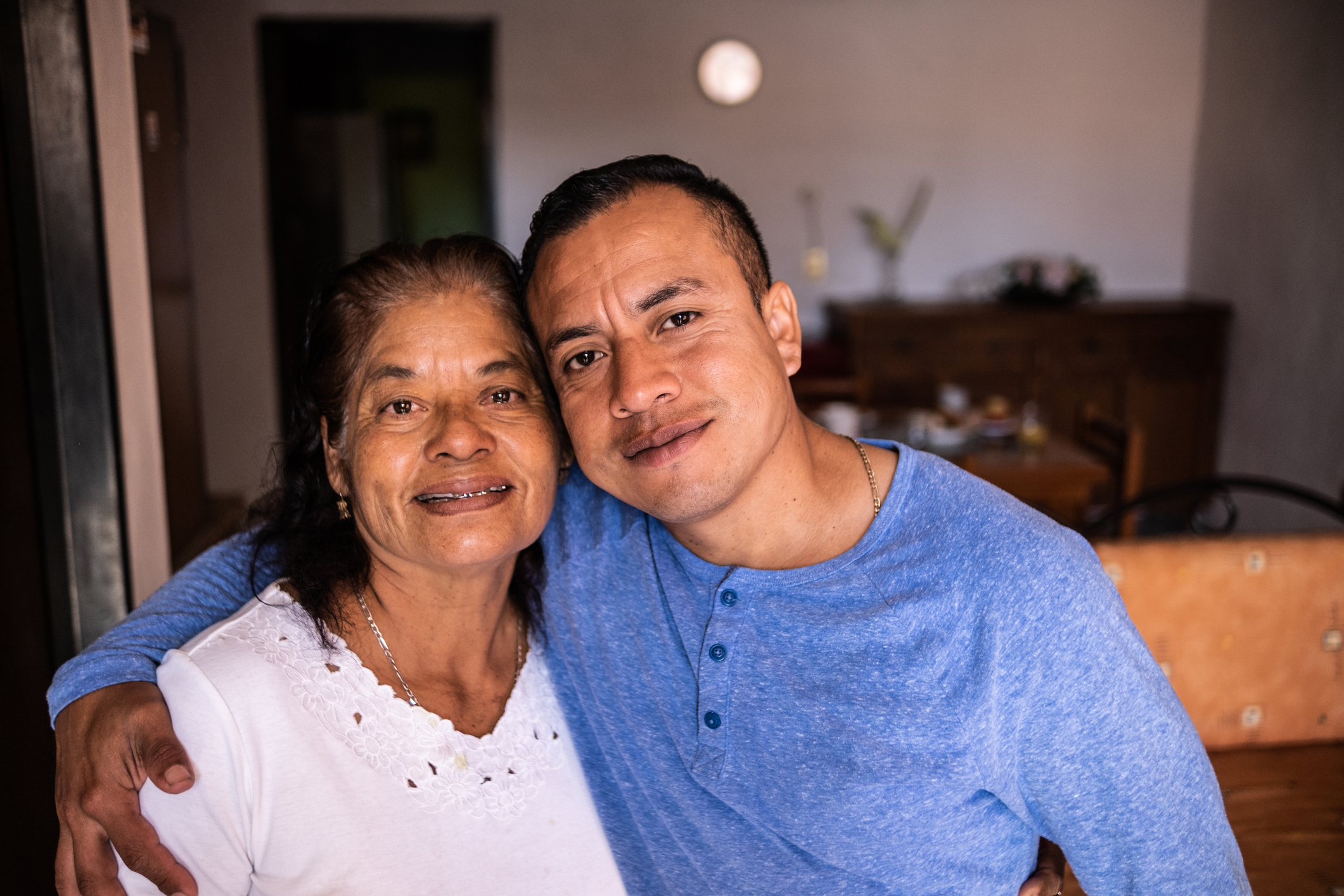 Woman and younger man smiling and embracing in a home kitchen