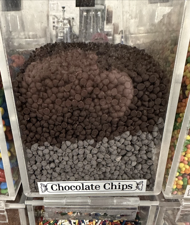 Bulk dispenser filled with chocolate chips, labeled at the bottom. Ideal for baking with kids