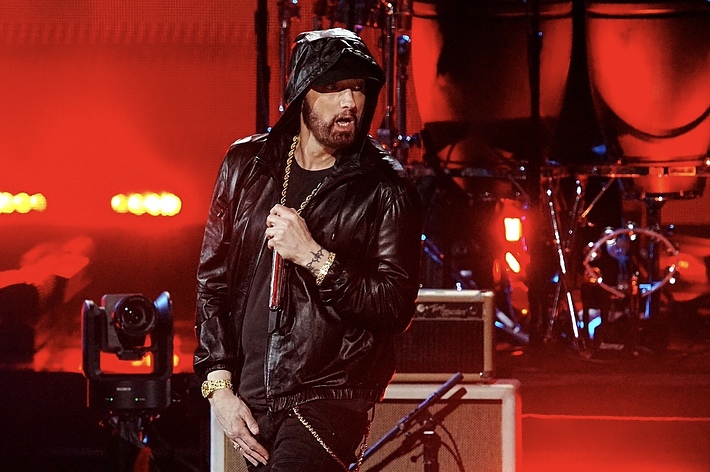 Eminem performing on stage, wearing a black leather jacket and holding a microphone