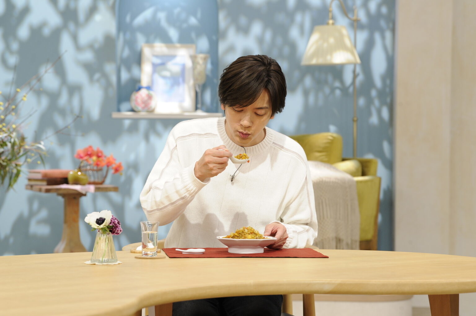 男性がテーブルでパスタを食べている。花の装飾がある。
