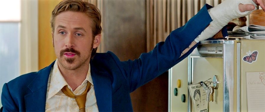 Ryan Gosling in a scene, wearing a blue jacket and a yellow tie, with a cast on his left arm
