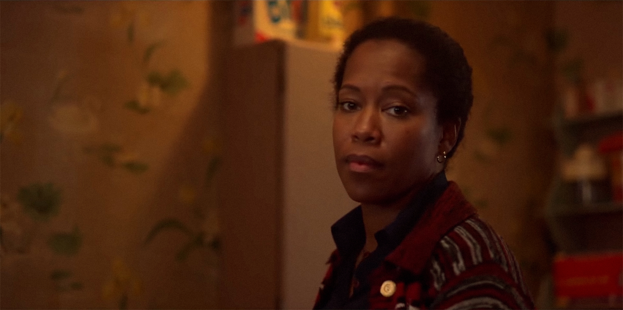 Regina in a striped jacket looking back over her shoulder indoors