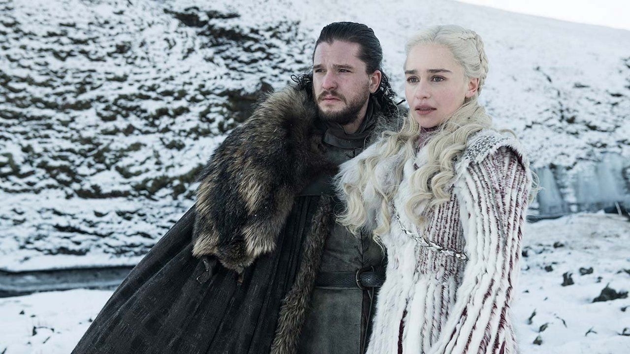 Jon Snow and Daenerys Targaryen from Game of Thrones standing in a snowy landscape, wearing warm, fur-lined winter clothing