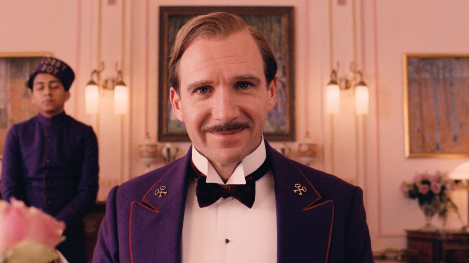 Ralph Fiennes in a concierge uniform standing in a hotel lobby from &quot;The Grand Budapest Hotel.&quot;