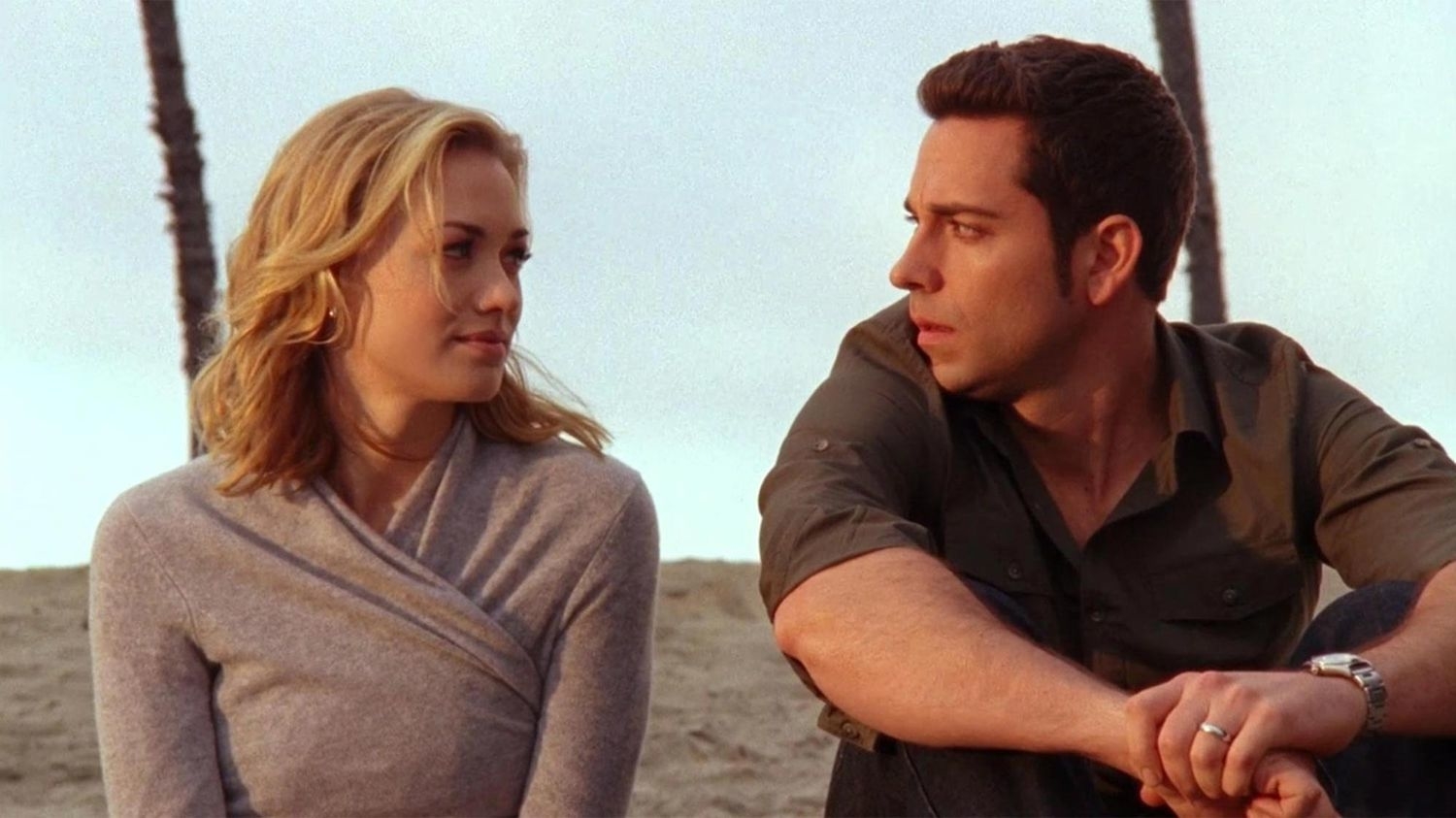 Two characters from a scene with a beach backdrop, sitting side by side, appear to be in conversation