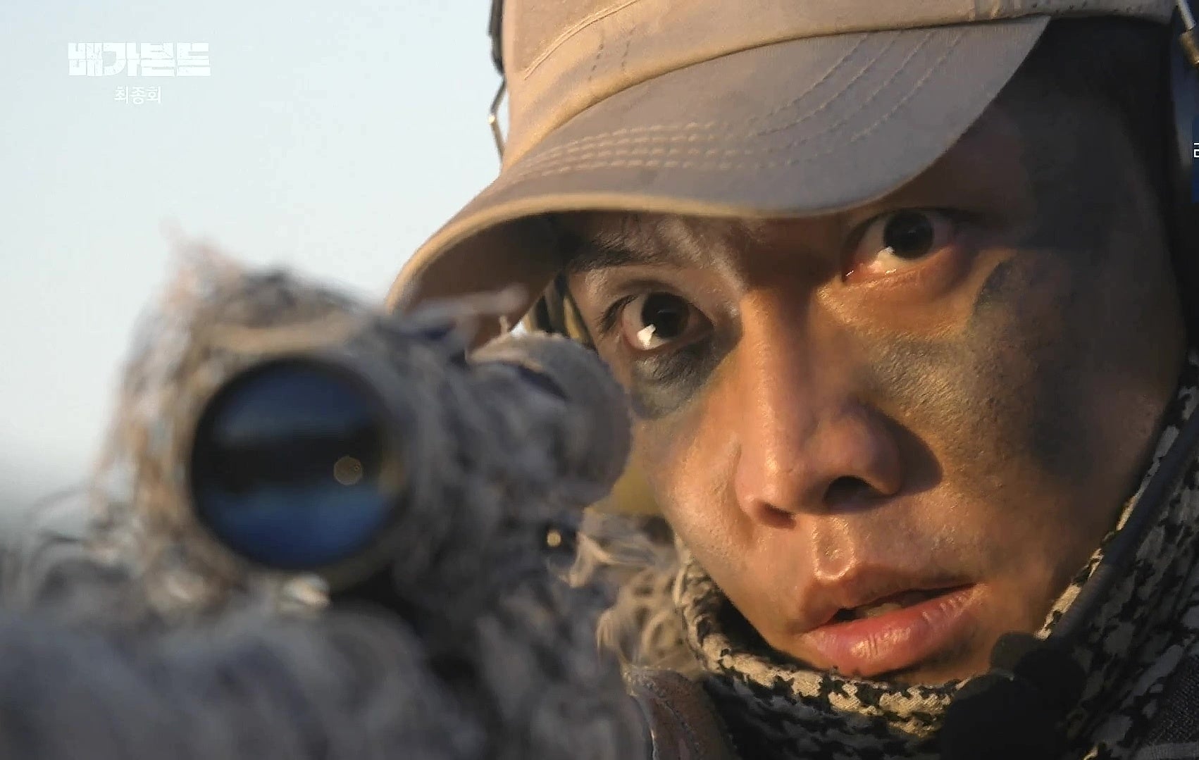 Close-up of a person in camouflage aiming a camera, expression focused
