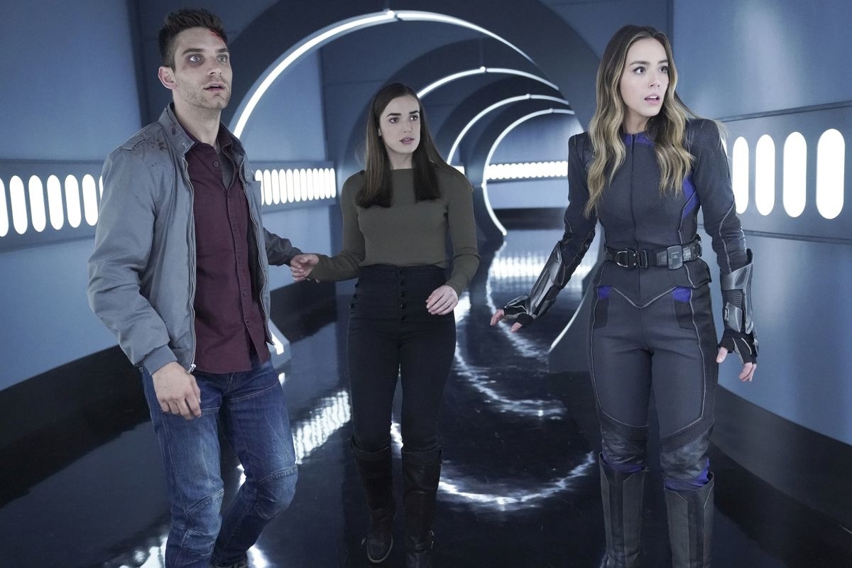 Three characters from the TV show walk together in a futuristic corridor, with tense expressions