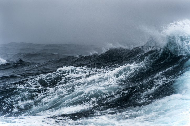 A rough sea with large, frothy waves under an overcast sky