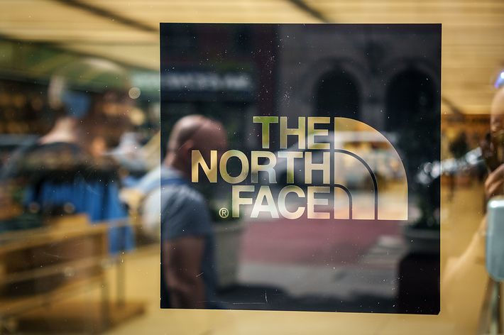 The North Face logo on a glass window with blurred figures and store interior visible in the background
