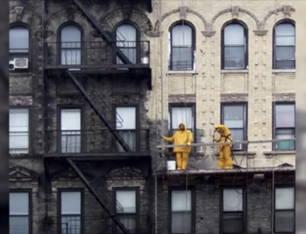 Two individuals in yellow raincoats on a building&#x27;s fire escape