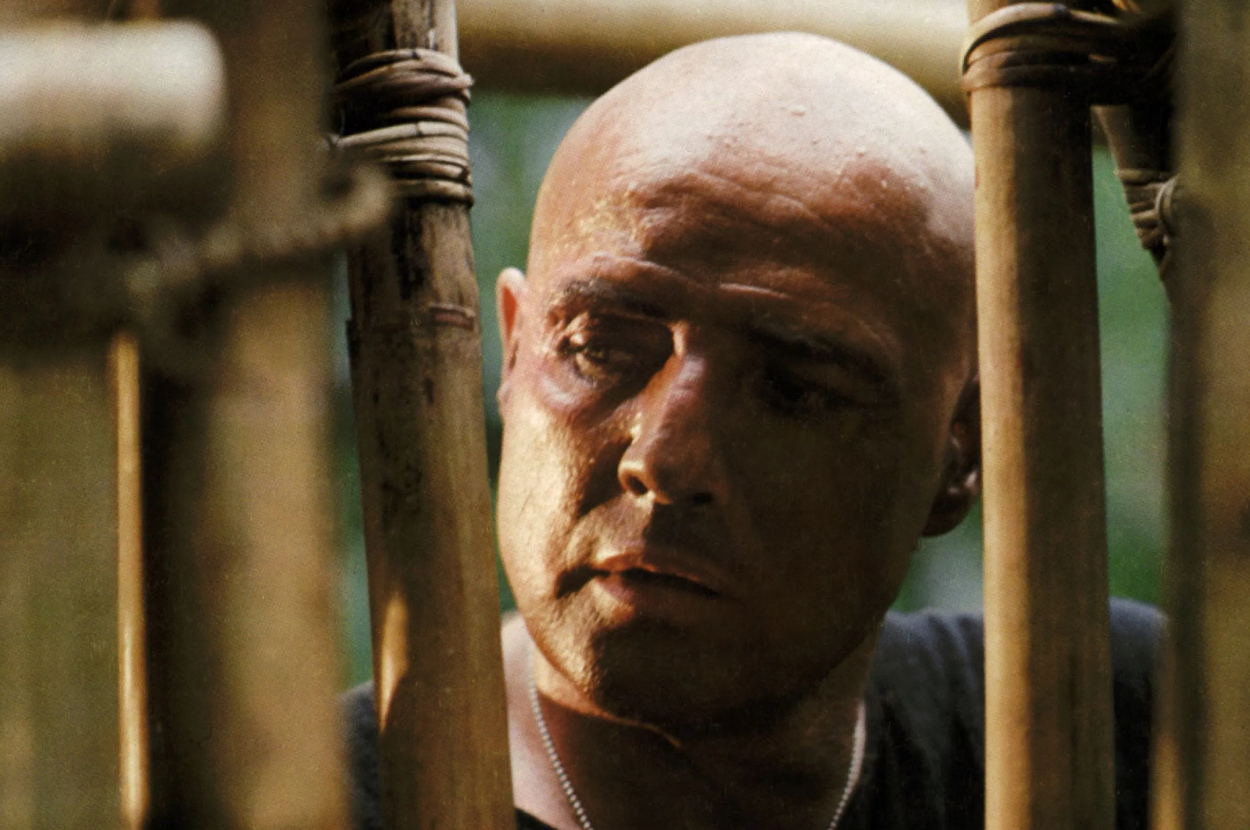 Man with a bald head looking intensely through wooden bamboo-like bars