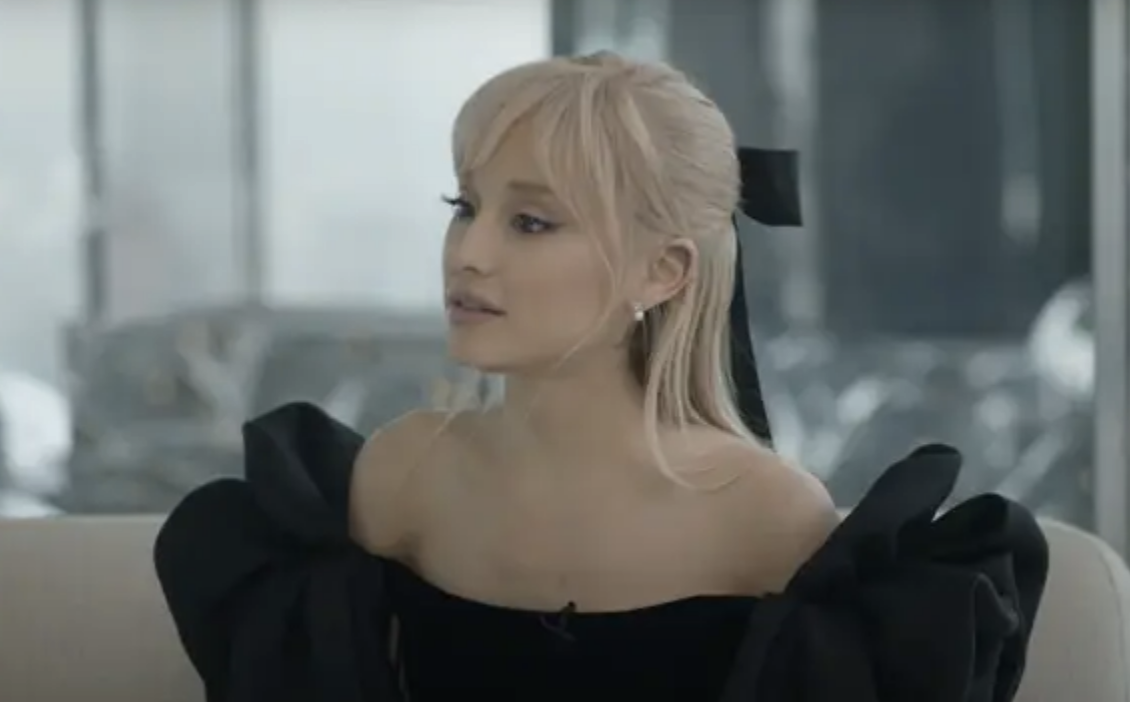 Ariana with an updo and off-shoulder ruffled top doing an interview