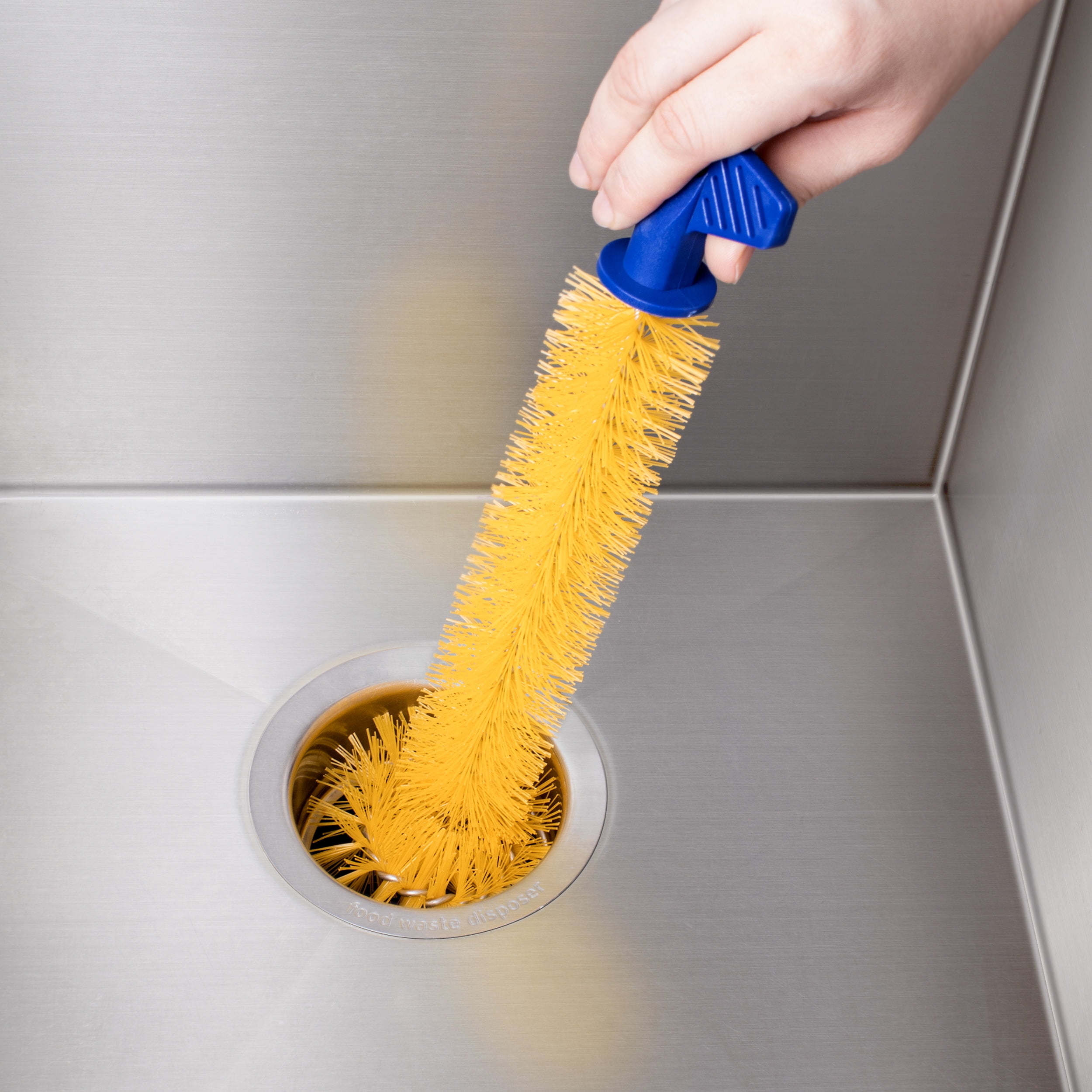 Hand using a yellow bristle brush for cleaning a stainless steel sink drain